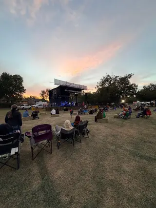 Residents seated on the lawn facing the Deutschen Pfest stage beneath a pink sunset