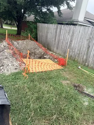 Open fiber construction pit in a Pflugerville yard with orange safety fencing and plywood cover