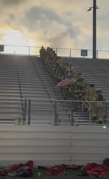 Firefighters in full gear carrying an American flag up stadium stairs during the September 11 memorial climb