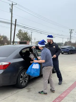 Jonathan Coffman and a Pflugerville public safety officer handing a holiday gift bag to a family