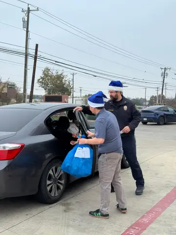 Jonathan Coffman and a Pflugerville public safety officer handing a holiday gift bag to a family