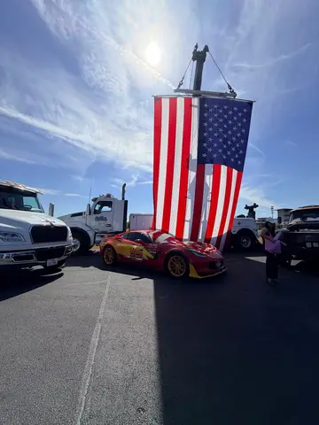 A large American flag suspended between tow trucks over a decorated car at Pflugerville Public Safety Day